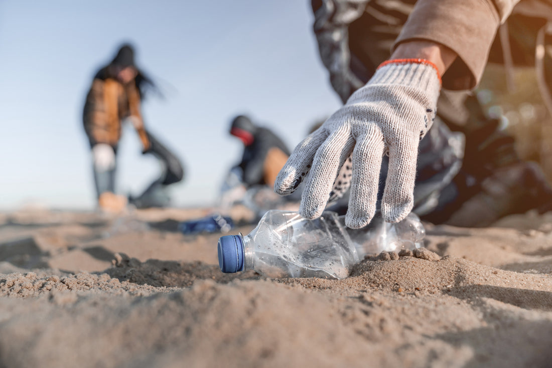 Person picking up plastic bottle while cleaning up the beach.